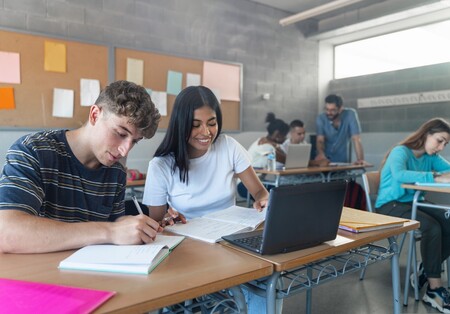 Online-Workshop für Schulen Zwei Schüler:innen sitzen im Klassenzimmer vor einem Laptop und lachen.
