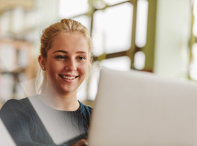 Beratung und Hilfe zu Künstlicher Intelligenz Eine junge Frau sitzt vor ihrem Laptop und lächelt.