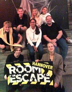 Die Scouts sitzen auf einer Treppe und halten ein Schild hoch auf dem "Room Escape" steht.