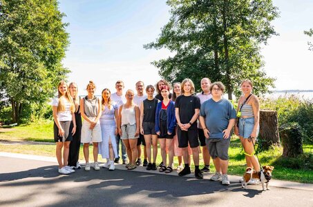 JUUUPORT-Scouts Eine Gruppe junger Menschen steht im Sommer vor einem See und schaut fröhlich in die Kamera.