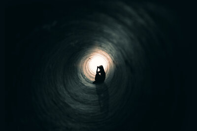 Eine junge Frau sitzt in einem dunklen Tunnel und sieht traurig aus.