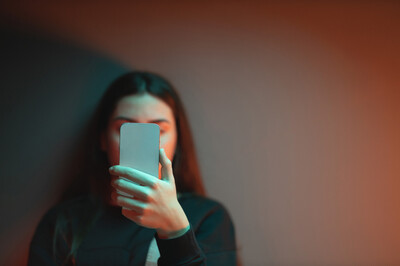 Künstliche Intelligenz im Alltag Ein Mädchen schaut auf ihr Smartphone - ihr Gesicht ist dahinter verborgen.