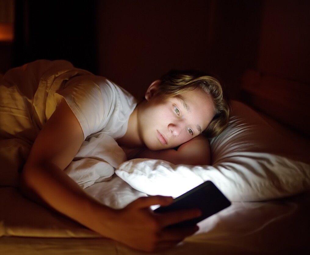 Jugendliche eigenes Handy Zeitpunkt Ein Junge liegt im Dunklen in seinem Bett und schaut auf das helle Handy-Display